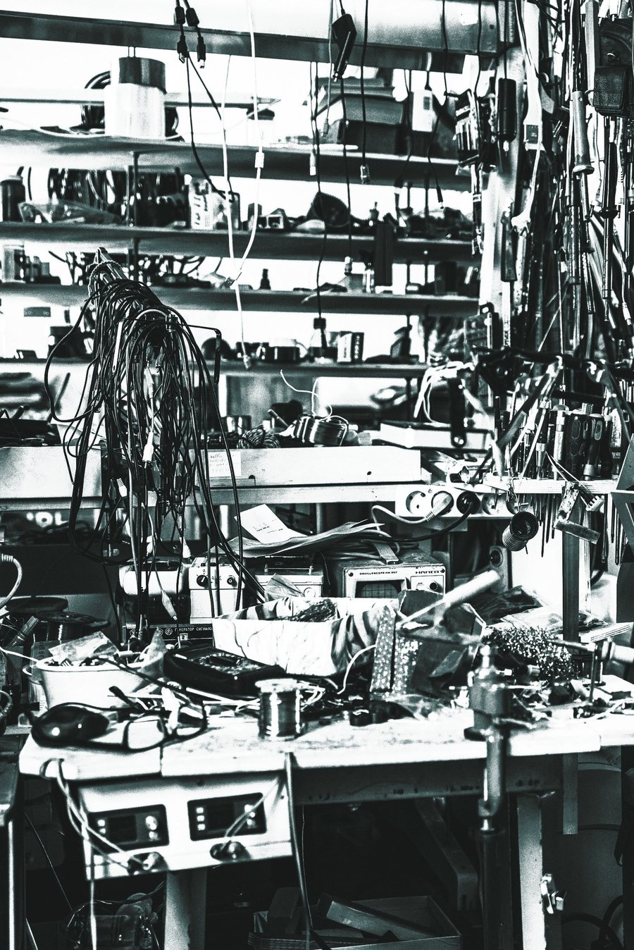 A crowded electronics workshop bench in teal duotone